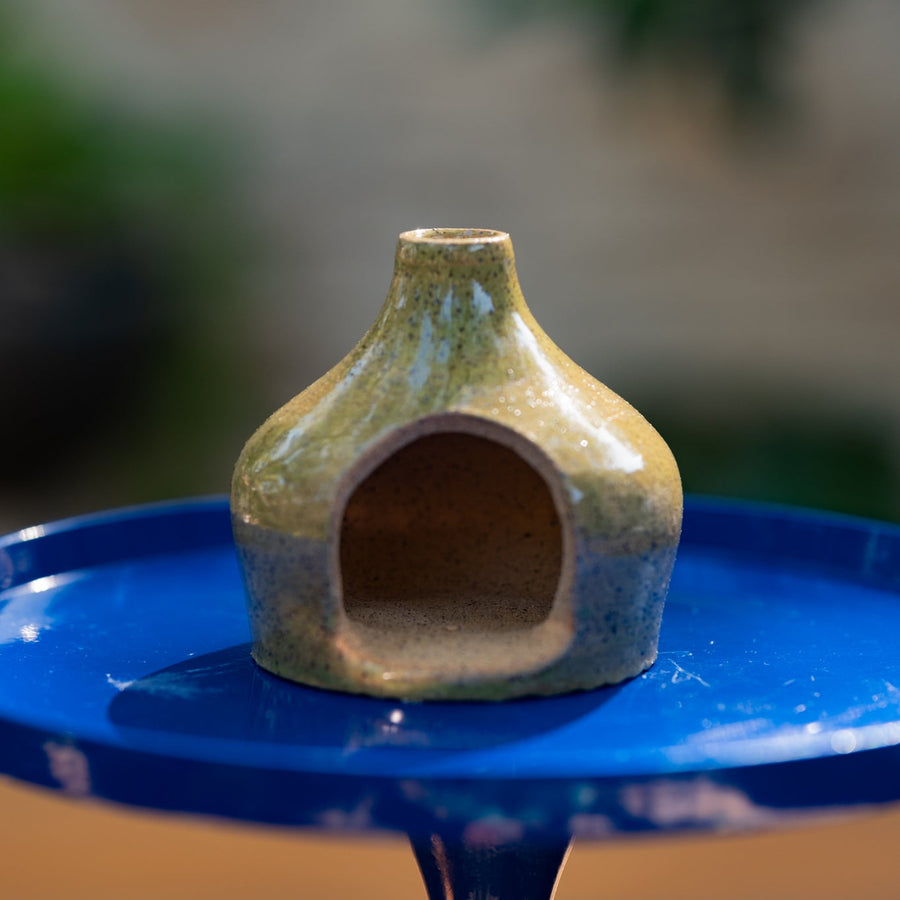 Small green ceramic mini chiminea on a blue stand with a blurred background