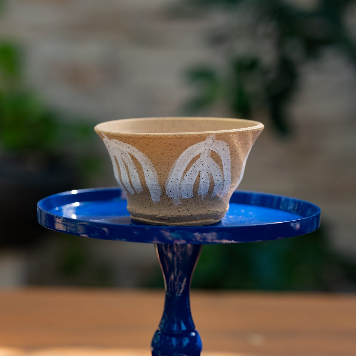 Ceramic planter with leaf patterns on a blue stand against a blurred natural background