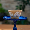 Ceramic planter with leaf patterns on a blue stand against a blurred natural background