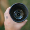 Hand holding a black ceramic cup with a blurred natural background
