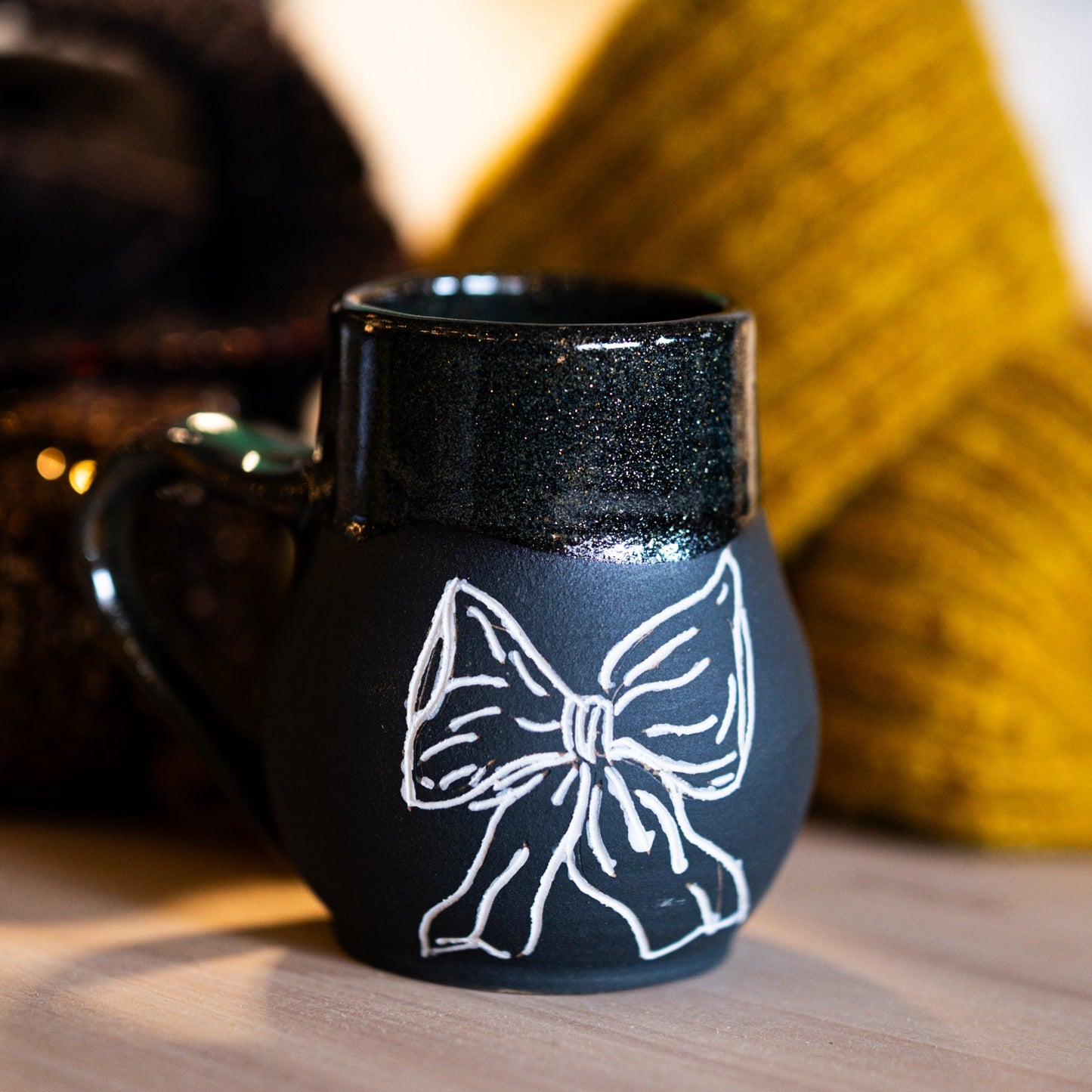 Black mug with a white bow design on a wooden surface